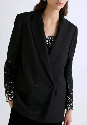 Zwarte op maat gemaakte blazer met een dubbelbreasted ontwerp, met gestructureerde mouwen versierd met zilveren studs, die een verloop-effect creëren.