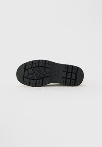 Suela de zapato de goma negra con surcos profundos y el logo "A|X Armani Exchange" grabado en el centro.