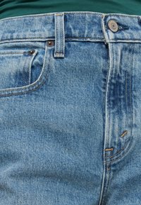 Ανοιχτό μπλε τζιν παντελόνι με πέντε τσέπες, ορείχαλκινα αξεσουάρ, ραφές σε τονικές αποχρώσεις και μια διακριτική υφή. Φθορές κοντά στις τσέπες.