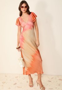 Maxi šaty v prechádzajúcich odtieňoch broskyne a koralu, s volánovými krátkymi rukávmi a voľnou siluetou. Doplnok tvorí ľahká taška.