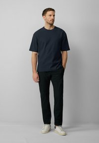 Navy gestructureerd shirt met korte mouwen, relaxte pasvorm, gecombineerd met zwarte slim-fit broeken en witte sneakers met groene accenten.
