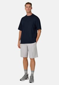 Marineblaues T-Shirt mit kurzen Ärmeln kombiniert mit hellgrauen Shorts, ergänzt durch graue Sportschuhe und gestreifte graue Socken. Schlichtes, entspanntes Design.