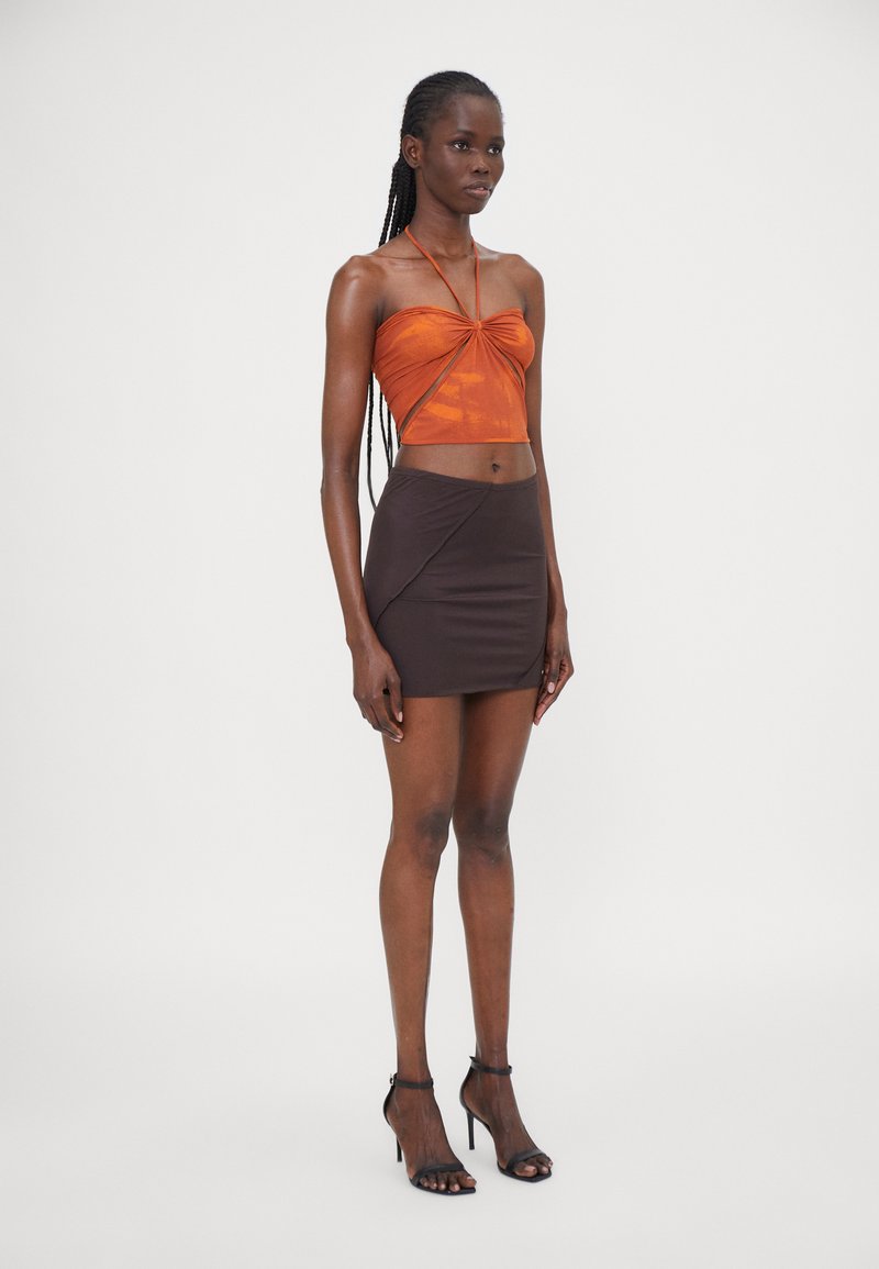 Orange cropped top with twisted design, paired with a fitted brown mini skirt. Model wears black strappy high-heeled sandals.