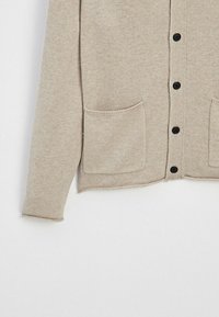 Beige gebreide cardigan met een ronde halslijn, vijf zwarte knopen en twee voorzakken. Zachte textuur met een ontspannen pasvorm en ribgebreide manchetten.