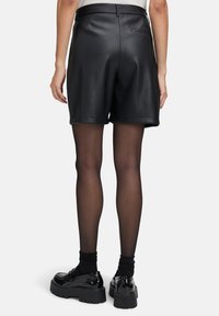 Zwarte leren shorts met een aansluitende taille en twee achterzakken, voorzien van een gladde textuur en een op maat gemaakte uitstraling. Combineer met schoenen met een dikke zool.