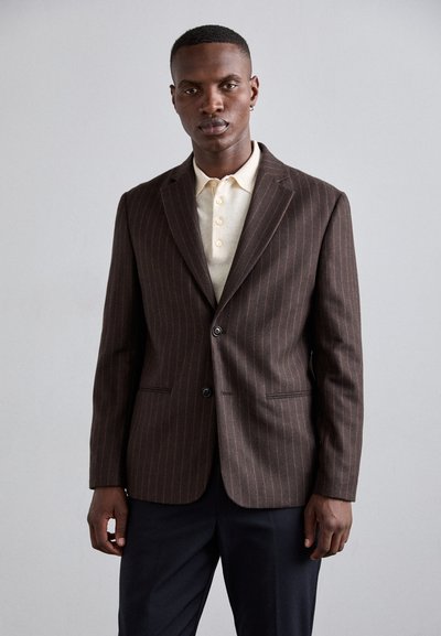 Blazer marron à rayures, avec un bouton unique, deux poches avant et un col cranté, superposé à un polo de couleur crème.