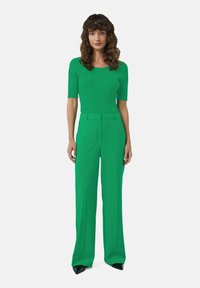 Haut en tricot côtelé vert à manches courtes associé à un pantalon taille haute à jambes larges assorti ; texture douce ; chaussures à bout pointu noires.