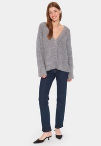 Gray knitted cardigan with a V-neck, front buttons, and ribbed texture, paired with dark blue slim-fit jeans and black heels.