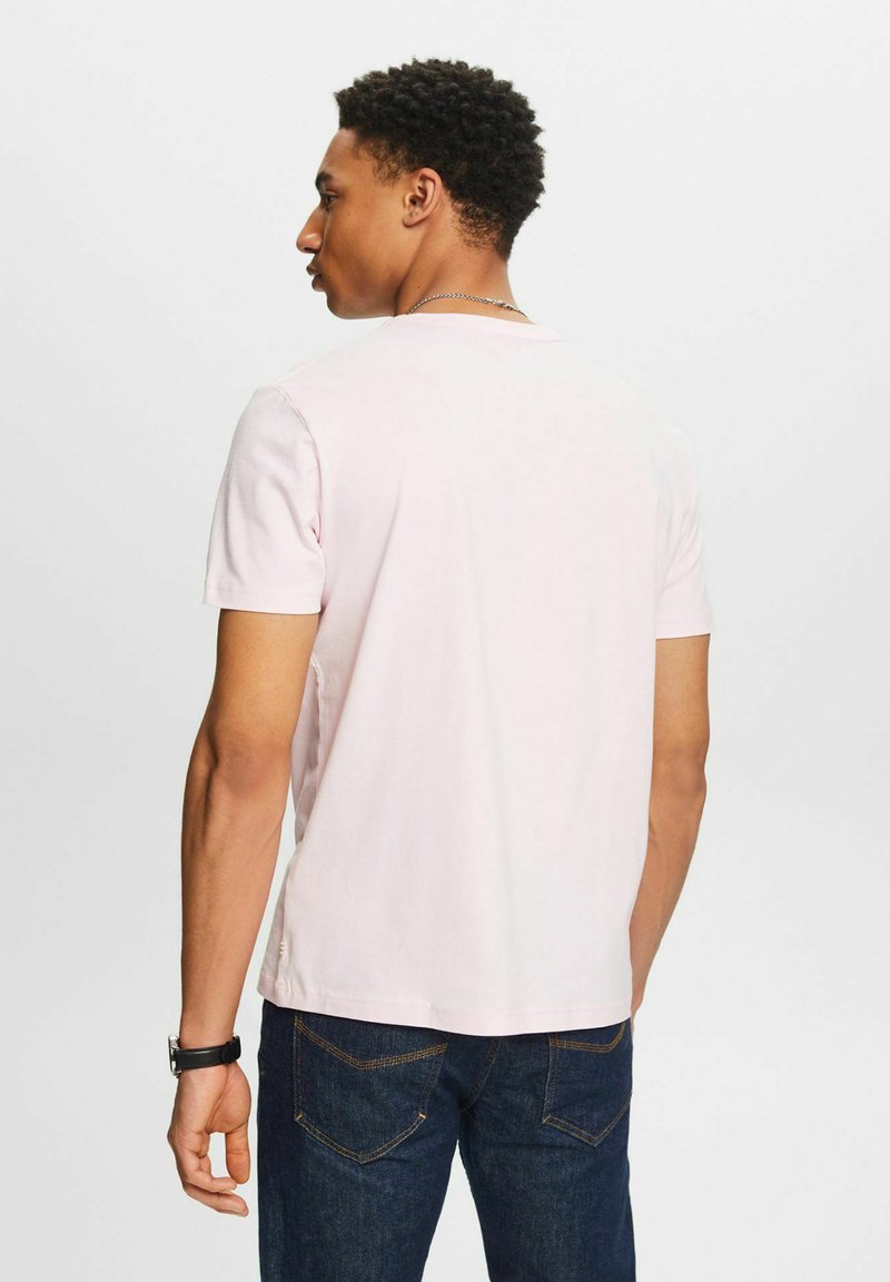 Kurzärmliges, hellrosa T-Shirt aus Baumwolle. Mit einem Rundhalsausschnitt und einer entspannten Passform. Kombiniert mit dunkelblauen Jeans.