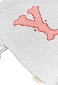 Acercamiento a una tela gris con un aplique en forma de coral rosa y dos pequeñas estrellas bordadas, mostrando parte de una etiqueta.