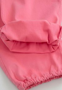 Jasnoróżowy materiał o miękkiej teksturze, z marszczoną gumą przy mankiecie, co zapewnia dopasowany krój. Gładkie szwy i jednolita kolorystyka.