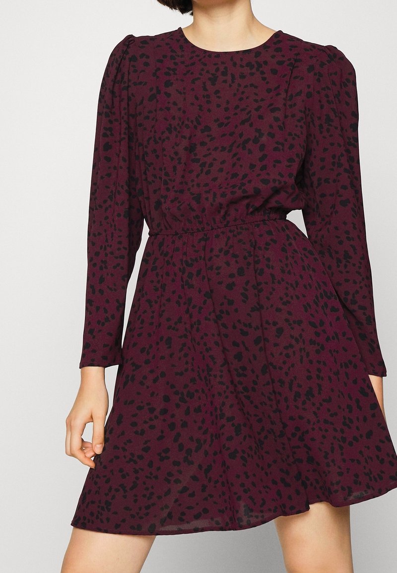 Robe bordeaux avec motif éclaboussé noir, manches longues, encolure ronde, taille cintrée et jupe évasée en ligne A. Tissu doux et léger.