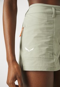 Ljusgröna shorts i mjukt material, med en orange dragsko, en vit logotyp på sidan, och en figurnära design med en jämn textur.