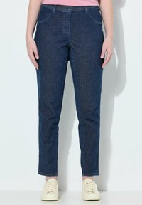 Džíny ve tmavě modré barvě, s rovnýma nohama, elastickým pasem, předními kapsami a hladkým povrchem. Kombinováno se světlými botami.