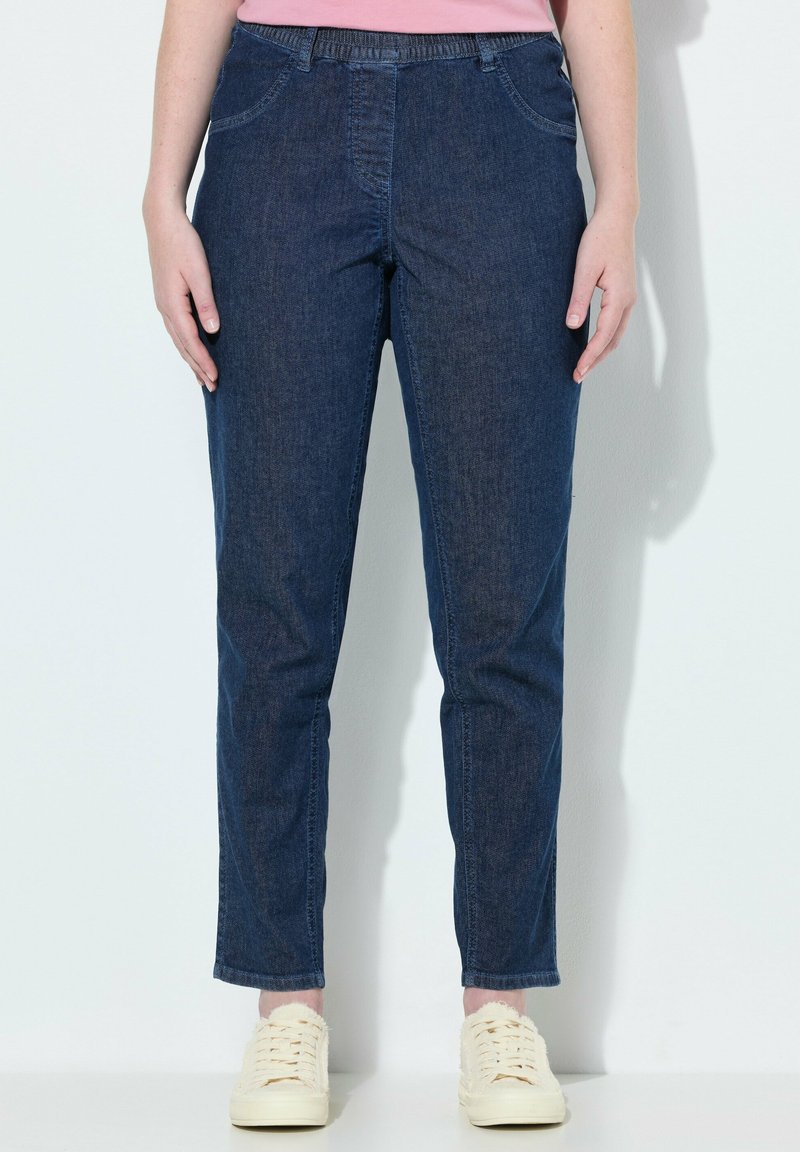 Džíny ve tmavě modré barvě, s rovnýma nohama, elastickým pasem, předními kapsami a hladkým povrchem. Kombinováno se světlými botami.