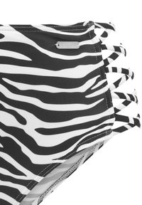 Schwarz-weißer Badestoff mit Zebra-Streifen und seitlichen Bindebändern. Hat eine glatte Textur und ein Metall-Logo mit dem Namen "Venice Beach."