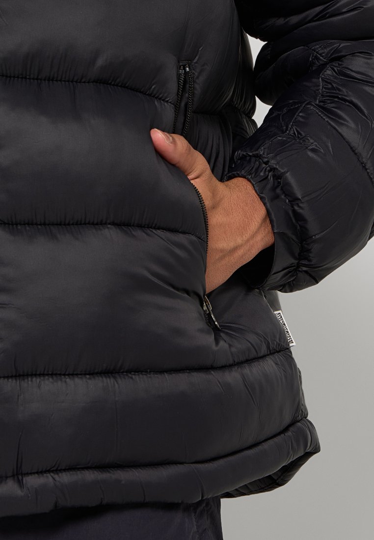 Veste matelassée noire dotée d'une poche zippée, d'un tissu extérieur texturé et de poignets élastiques. Conçue pour tenir chaud avec une silhouette volumineuse.