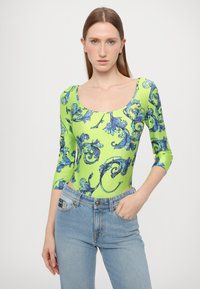 Grønn langermet body med blå blomstermønstre, rund hals, parret med lyseblå denimjeans. Glatt stofftekstur.
