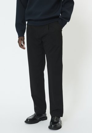 Pantalon noir sur mesure à coupe droite, poches latérales et texture lisse, assorti à des chaussures noires et un pull bleu marine.