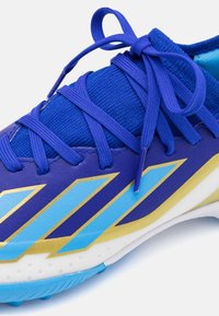 Scarpa sportiva blu con una tomaia testurizzata, caratterizzata da un design blu e oro, lacci testurizzati e una suola blu a contrasto.