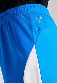 Ljusblå sportshorts med en vit sidpanel och andningsbar meshmidja, försedd med en "DRY"-logotyp.