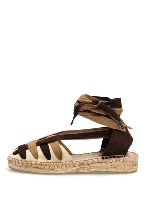 Sandalia plana tipo espadrille con tiras de tela beige y marrón oscuro y lazos en el tobillo sobre una suela de yute trenzado.