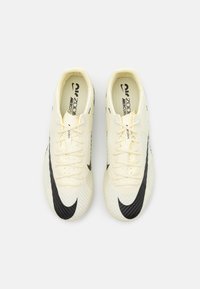 Botas de fútbol de color crema claro con un patrón texturizado, acento de swoosh negro y cordones tradicionales. Incluye una plantilla acolchada para mayor comodidad.