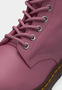 Gros plan d'une botte en cuir rose avec des lacets assortis passés dans des œillets métalliques et une couture jaune visible sur la semelle marron.