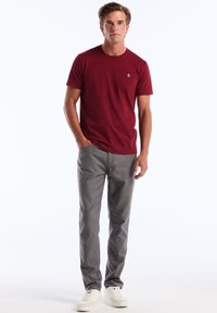 Bordeaux crew-neck t-shirt met korte mouwen, gecombineerd met lichtgrijze broek en witte sneakers. Casual pasvorm met minimale branding.