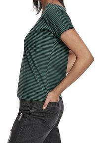 Zelené pruhované tričko s krátkým rukávem, volného střihu a kulatým výstřihem. Materiál vypadá měkce a má hladký povrch.