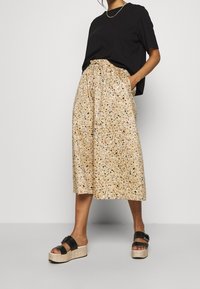 Bežová sukně se vzory a skvrnami modré a hnědé, se strečovým pasem a bočními kapsami, doplněná černými platformovými sandály.
