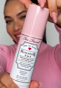 Too Faced Hangover 3-in-1 primer and setting spray. White bottle with pink cap, gold accents, and black label. Contains coconut water, 120ml.