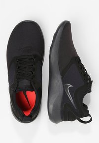 Zapatillas deportivas negras con parte superior textil lisa, interior rojo contrastante, suela acolchada y detalle sutil de logo en el lateral.