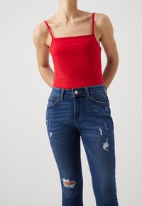 Červený přiléhavý top na ramínka s úzkými ramínky, doplněný o roztrhané modré džínové kalhoty s otvory a klasickým pětikapsovým designem.
