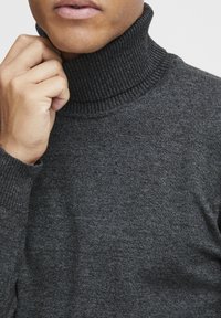 Suéter gris de cuello alto hecho de tejido de punto texturizado, que presenta un cuello acanalado alto y un diseño ajustado alrededor del cuello.