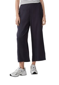 Marineblauwe loszittende cropped broek met een soepele textuur, voorzien van een elastische tailleband, gecombineerd met witte sportschoenen.