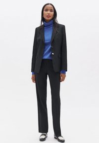 Saco y pantalones negros a medida con un cuello de tortuga azul. El conjunto presenta tejidos suaves, líneas estructuradas y colores contrastantes.