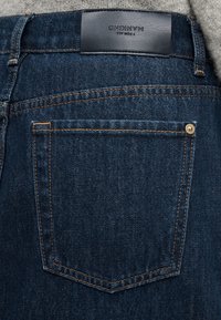 Τζιν από τζιν ύφασμα με σκούρο ξεβάφτισμα, διακοσμημένα με πορτοκαλί ραφές. Στη μέση υπάρχει καφέ δερμάτινο έμπλαστρο, με ένα μικρό χρυσό καρφίτσα στην τσέπη.