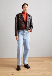 Veste de moto en cuir noir coupée avec quincaillerie argentée, col roulé rouge, jeans droit bleu clair, et bottes noires à plateforme.