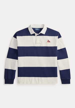 Dwa modele noszą granatowo-białe, paskowane koszulki rugby; jeden w podartych dżinsach i sandałach, drugi w białych spodniach, trampkach i okularach przeciwsłonecznych.