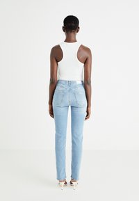 Vaqueros de denim azul claro con corte ajustado, cintura alta y dos bolsillos traseros. Combinados con una blusa blanca sin mangas. Diseño simple y minimalista.