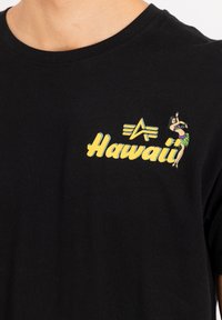 Čierne bavlnené tričko s žltým potlačou "Hawaii", abstraktným hviezdovým logom a farebnou grafikou tanečnice hula na ľavej strane hrude.