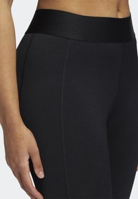 Collants de sport noirs avec une large ceinture texturée et des coutures le long des côtés, fabriqués dans un tissu extensible et évacuant l'humidité.