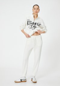 Witte cropped sweatshirt met een kwart-rits en zwarte opdruk "ATLANTIC City", gecombineerd met bijpassende witte joggingbroek en casual sneakers.
