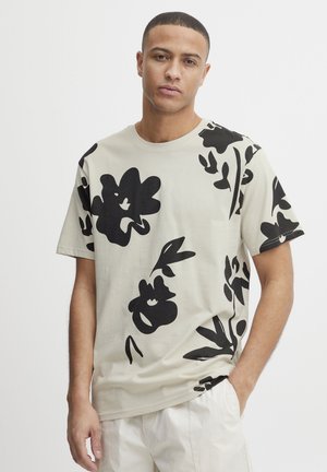 Lichtbeige t-shirt met grote zwarte bloemenprints aan één zijde. Gemaakt van zachte stof met een relaxte pasvorm en een ronde hals.