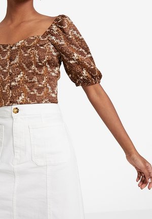 Brown snake print puff sleeve cropped top paired with a high-waisted white skirt featuring large front pockets and a button closure.