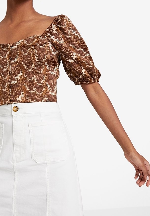 Haut court à manches bouffantes avec imprimé serpent marron, associé à une jupe blanche taille haute dotée de grandes poches avant et d'une fermeture par boutons.
