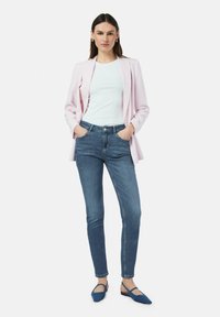Lichtroze blazer, witte getailleerde top, blauwe skinny jeans en blauwe ballerina's; gladde stof, taillering en subtiele kleurcontrast.
