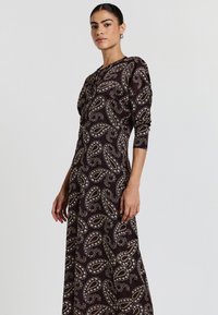 Abito lungo realizzato in morbido tessuto scuro, con un motivo paisley in crema e oro. Le maniche lunghe e il collo rotondo completano il design.