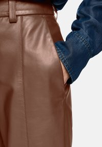 Brown leather pants with a smooth texture, featuring side pockets and a tailored fit, paired with a dark blue denim shirt.